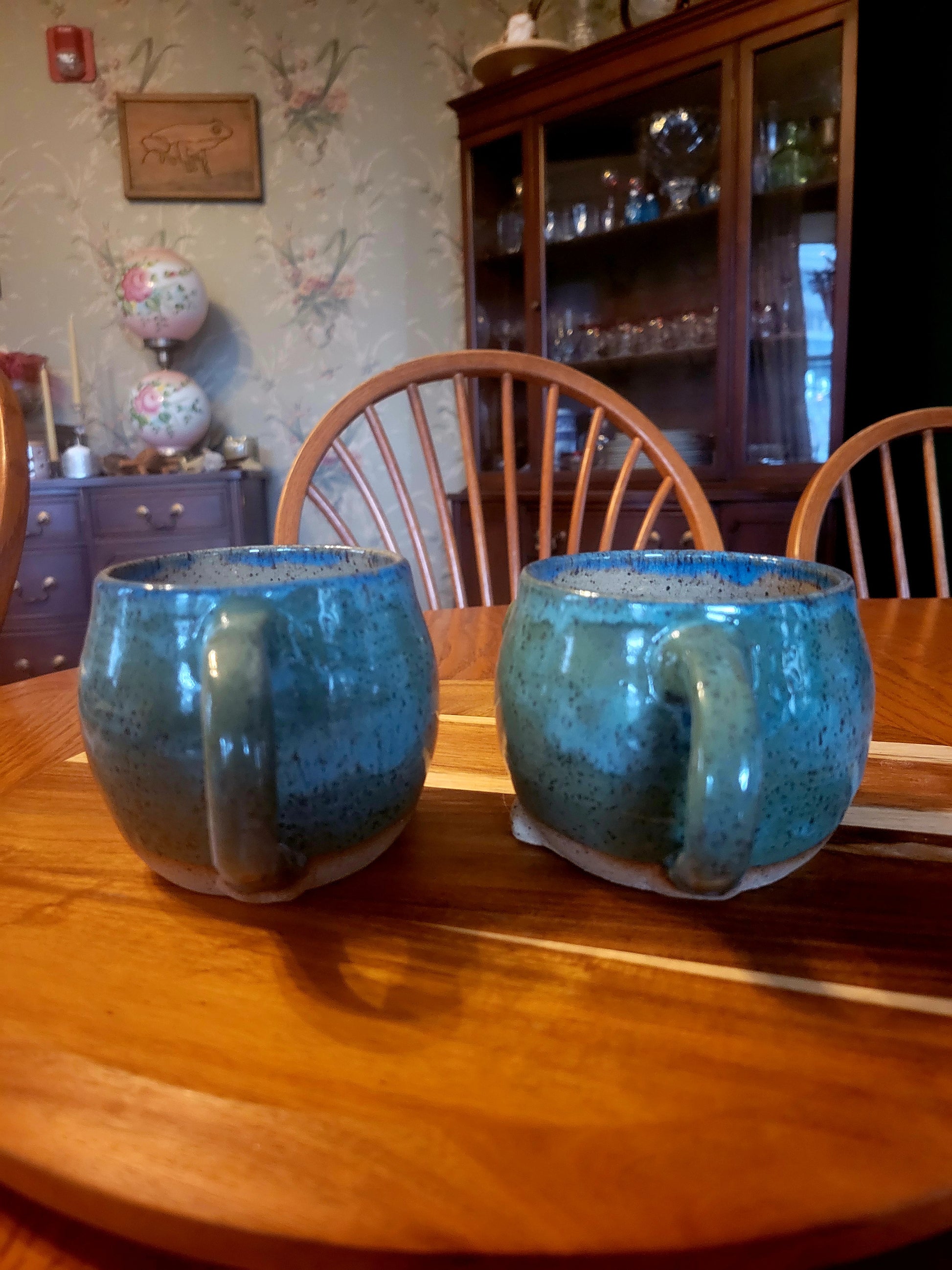 Two blue ceramic mugs on a wooden table with a background of a room with furniture and decor.