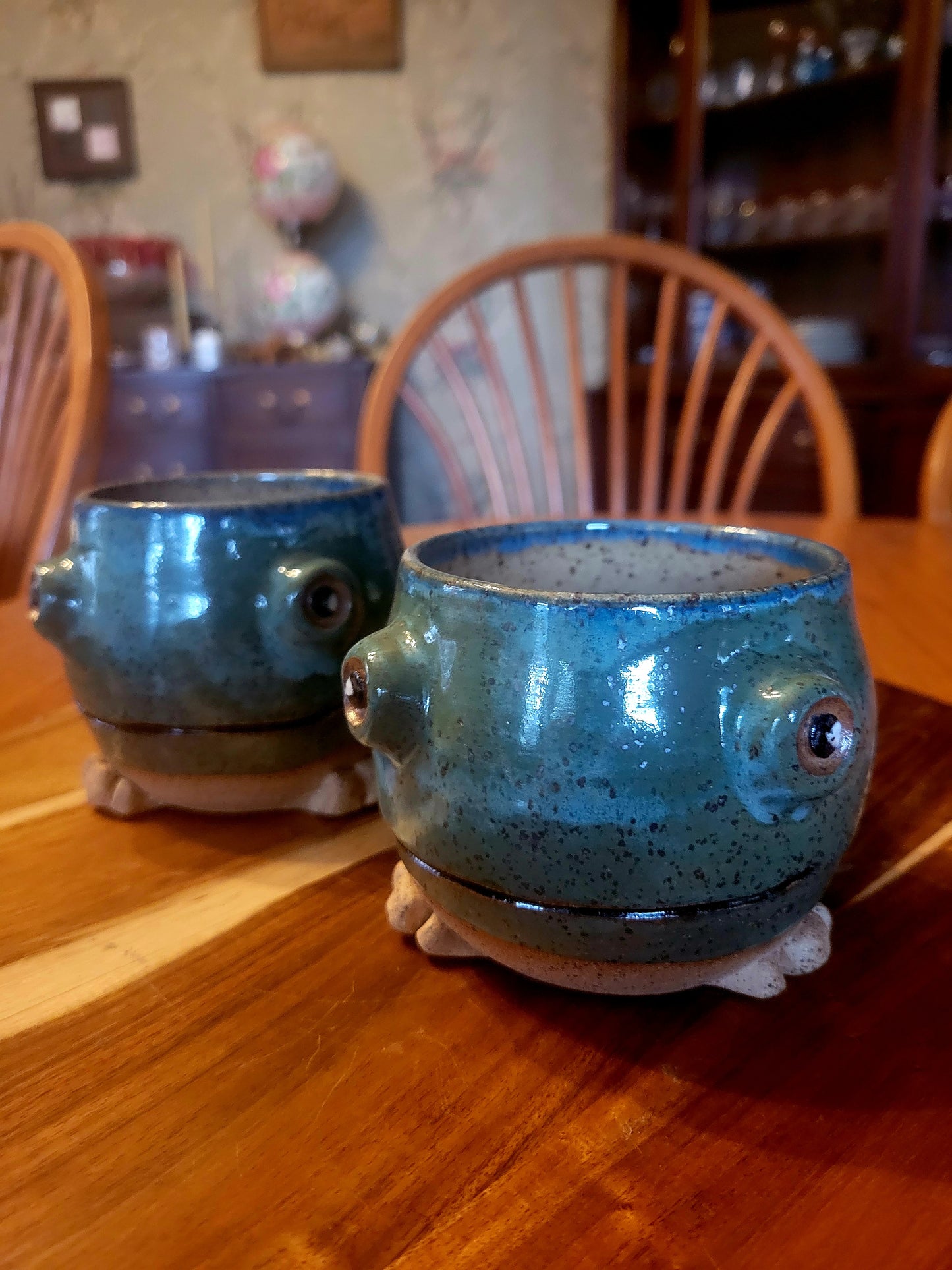 Two blue ceramic pots with frog-like faces on a wooden table.