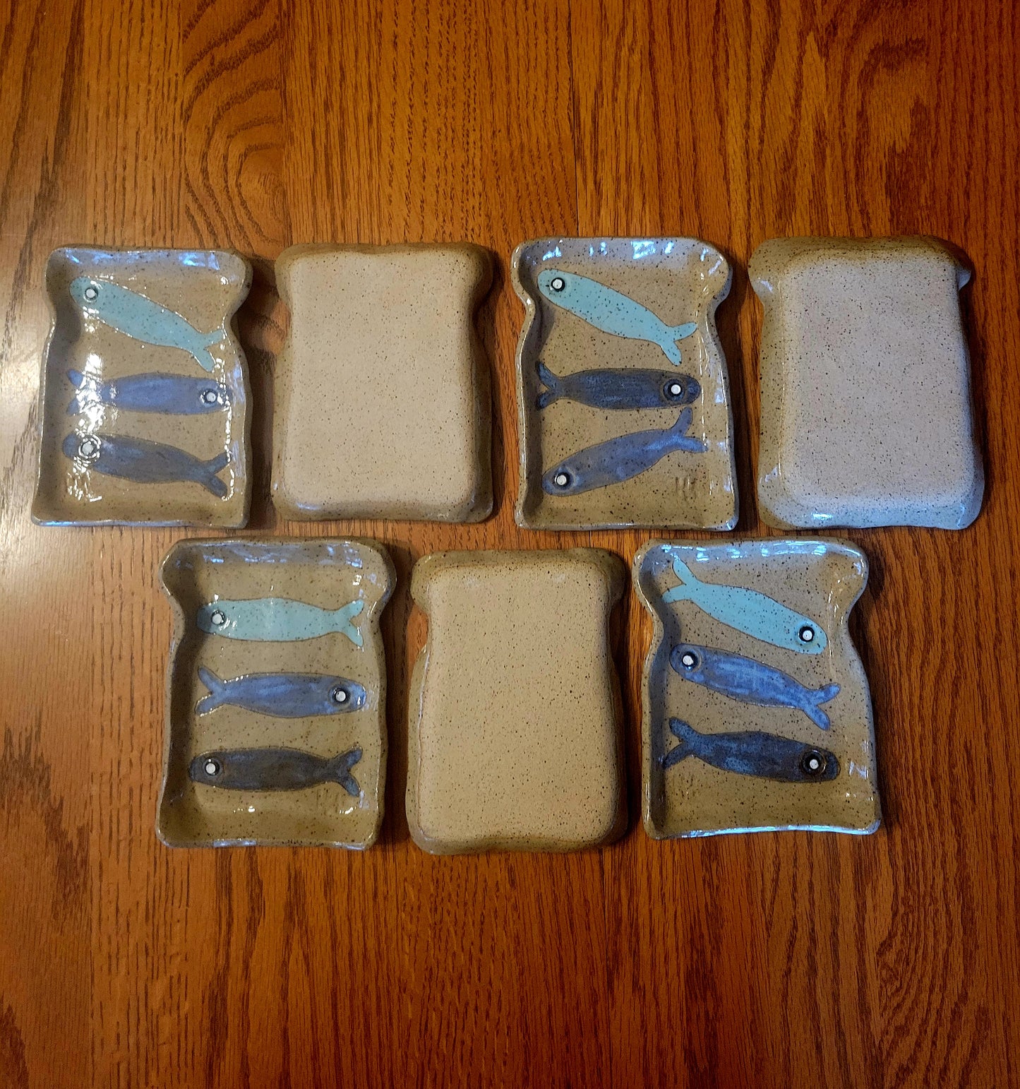 Set of ceramic toast-shaped plates with fish designs on a wooden surface
