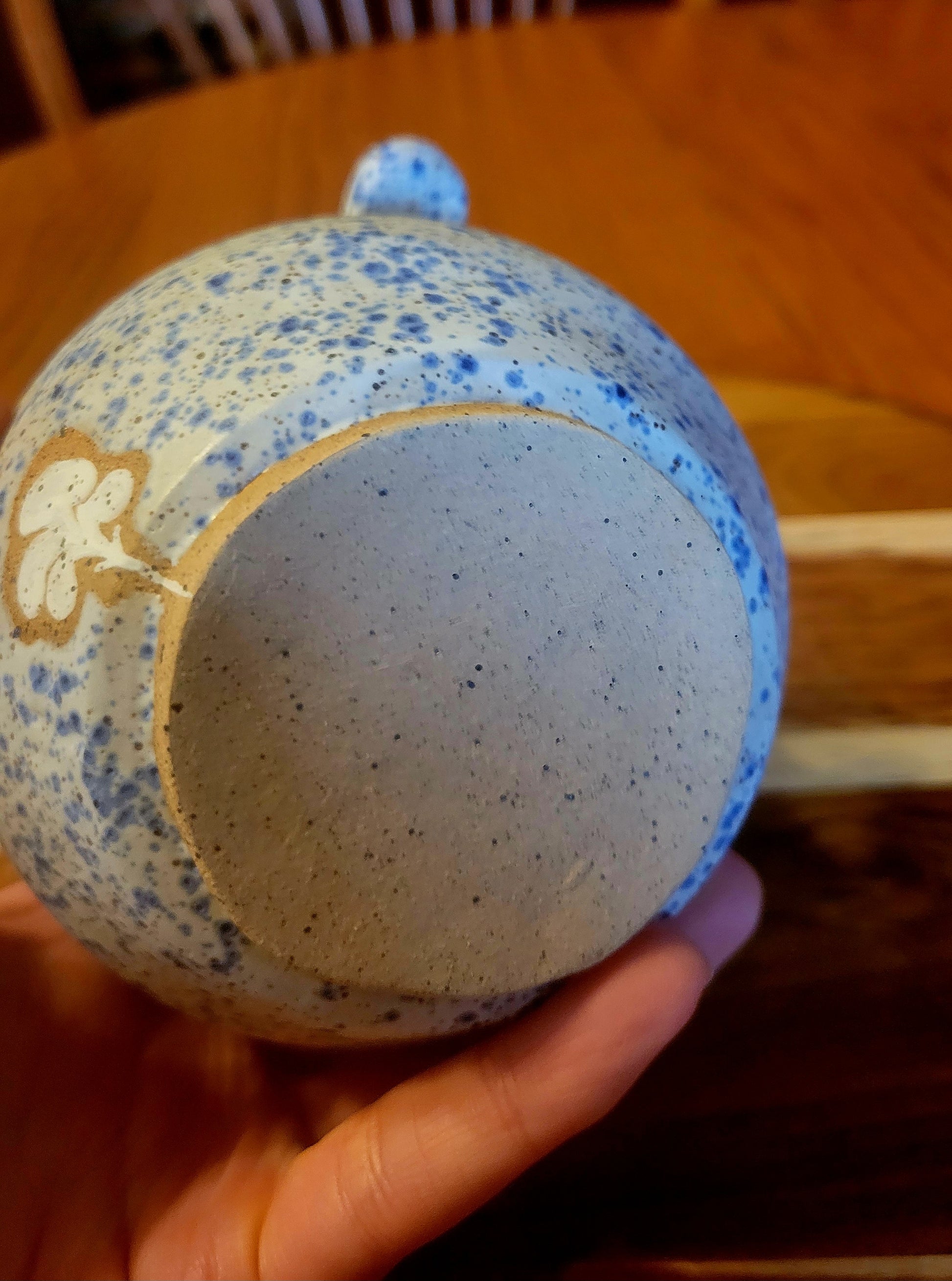 Ceramic container with blue speckles held by a hand on a wooden surface