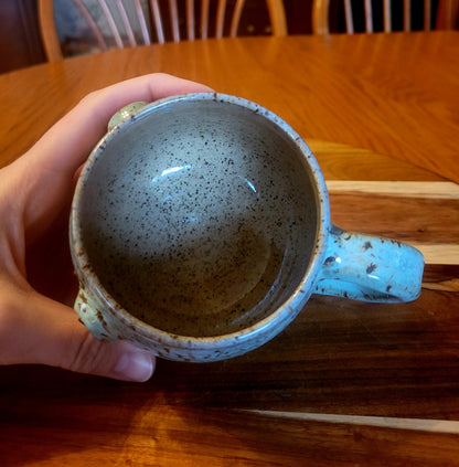 Hand holding a ceramic mug with speckled design on a wooden table.