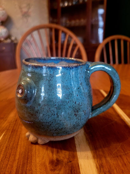 Blue ceramic mug shaped like a frog on a wooden table