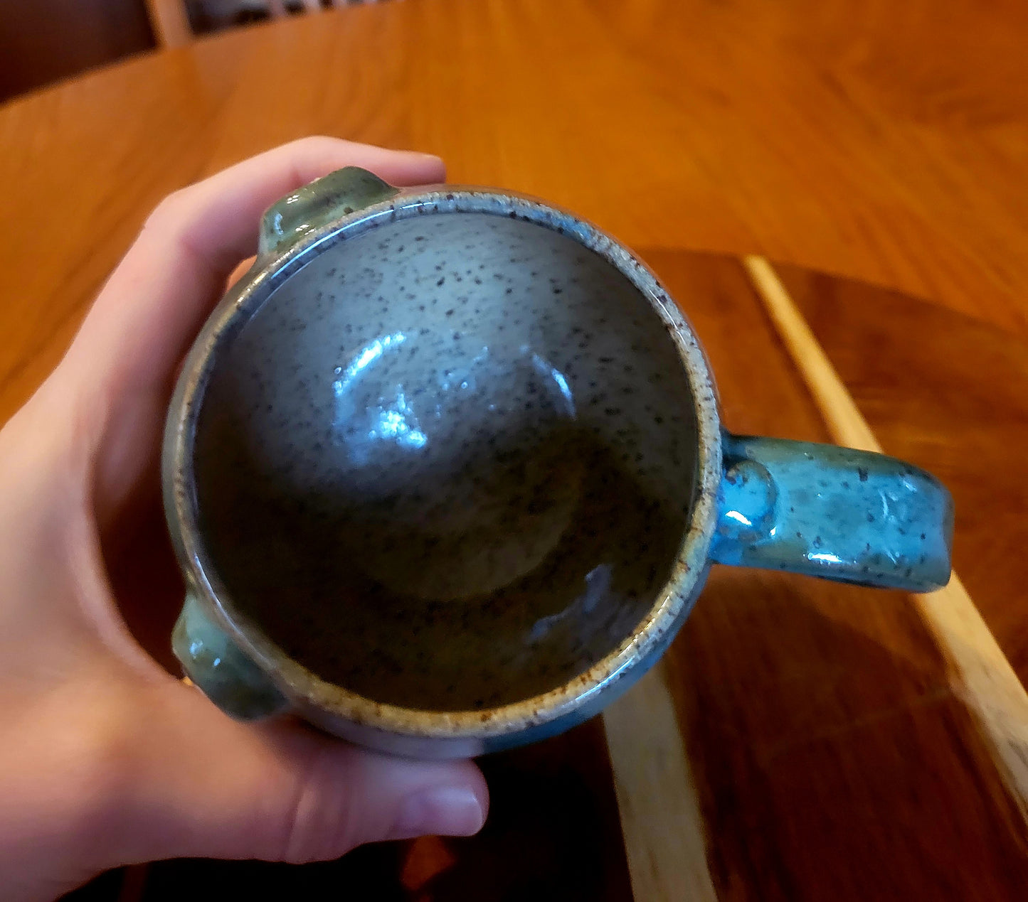 Hand holding a ceramic mug with a speckled design on a wooden table.