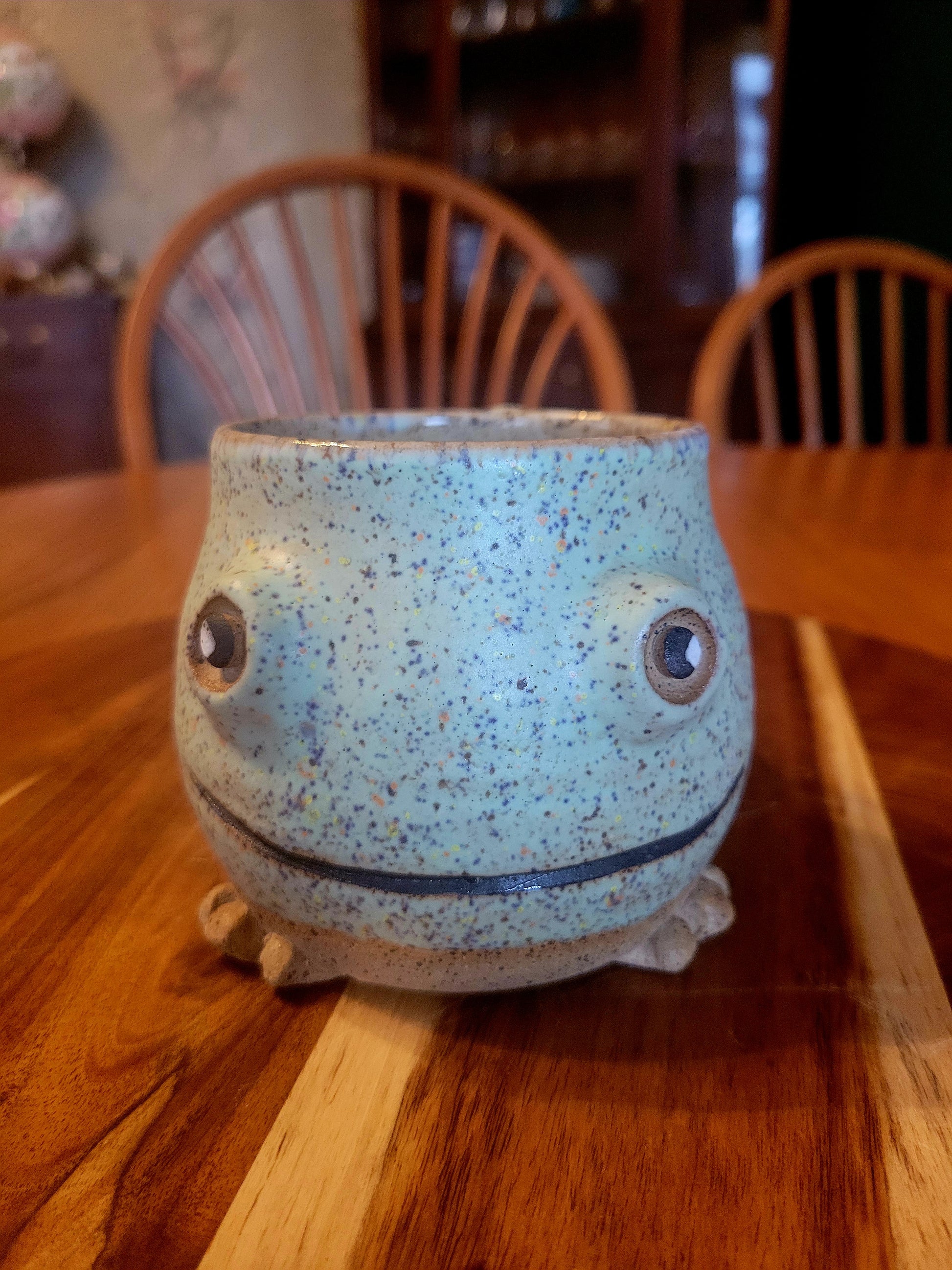 Speckled blue ceramic mug with face on a wooden table