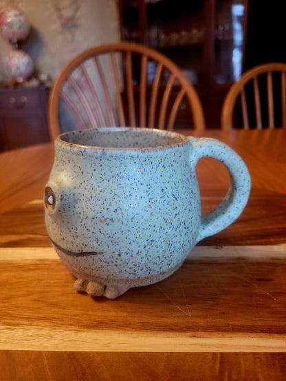 Speckled blue mug with a face on a wooden table
