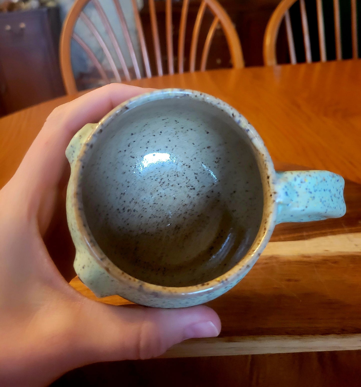 Hand holding a ceramic mug with a speckled design on a wooden table.