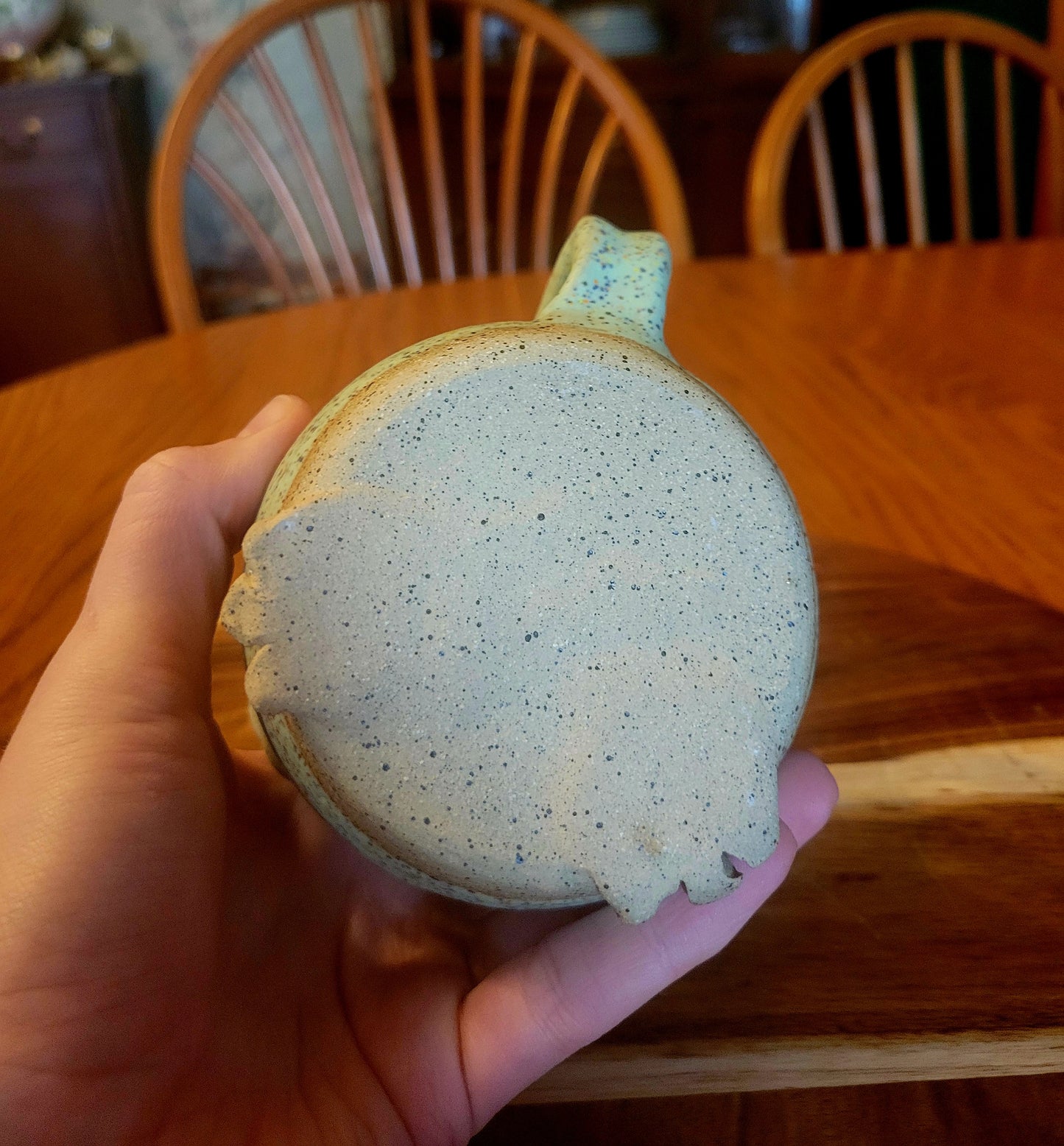 Hand holding a speckled blue and beige mug on a wooden table with chairs in the background.