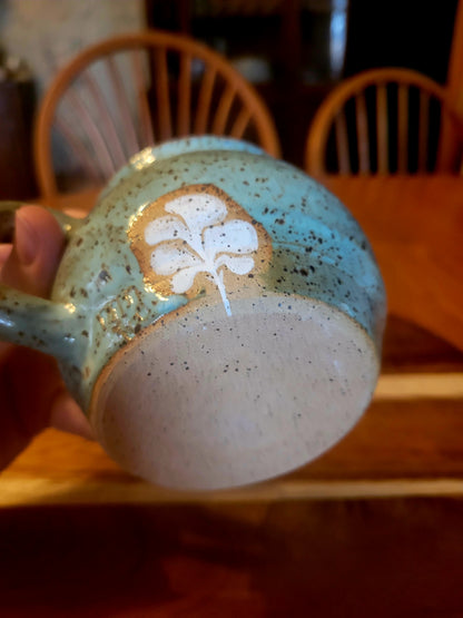 Ceramic mug with speckled design and white floral pattern held by a hand.