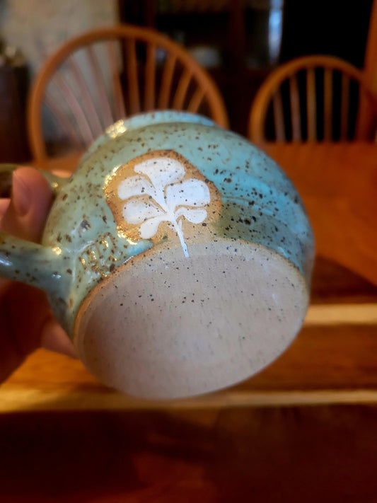 Ceramic mug with speckled design and white floral pattern held by a hand.