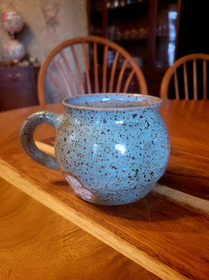 Blue speckled mug on a wooden table with chairs in the background