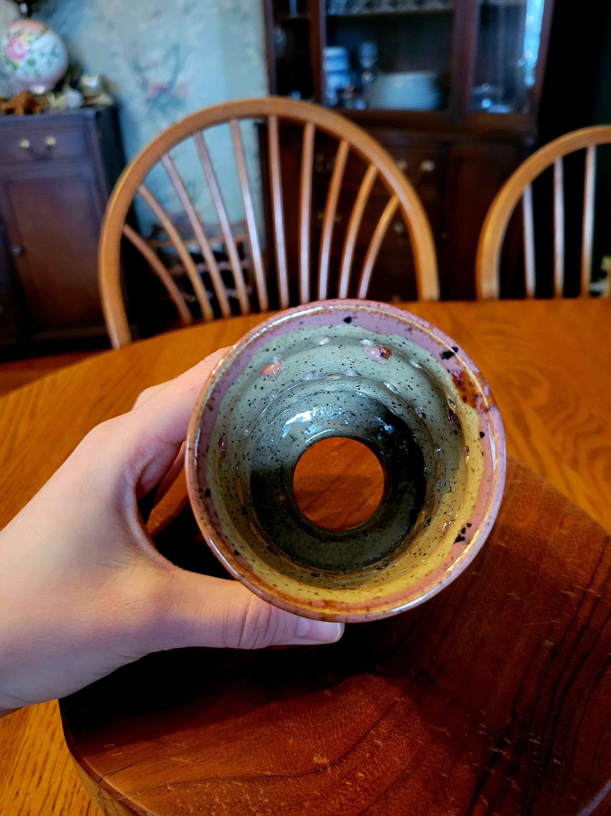 Hand holding a ceramic cup with a wooden table and chairs in the background