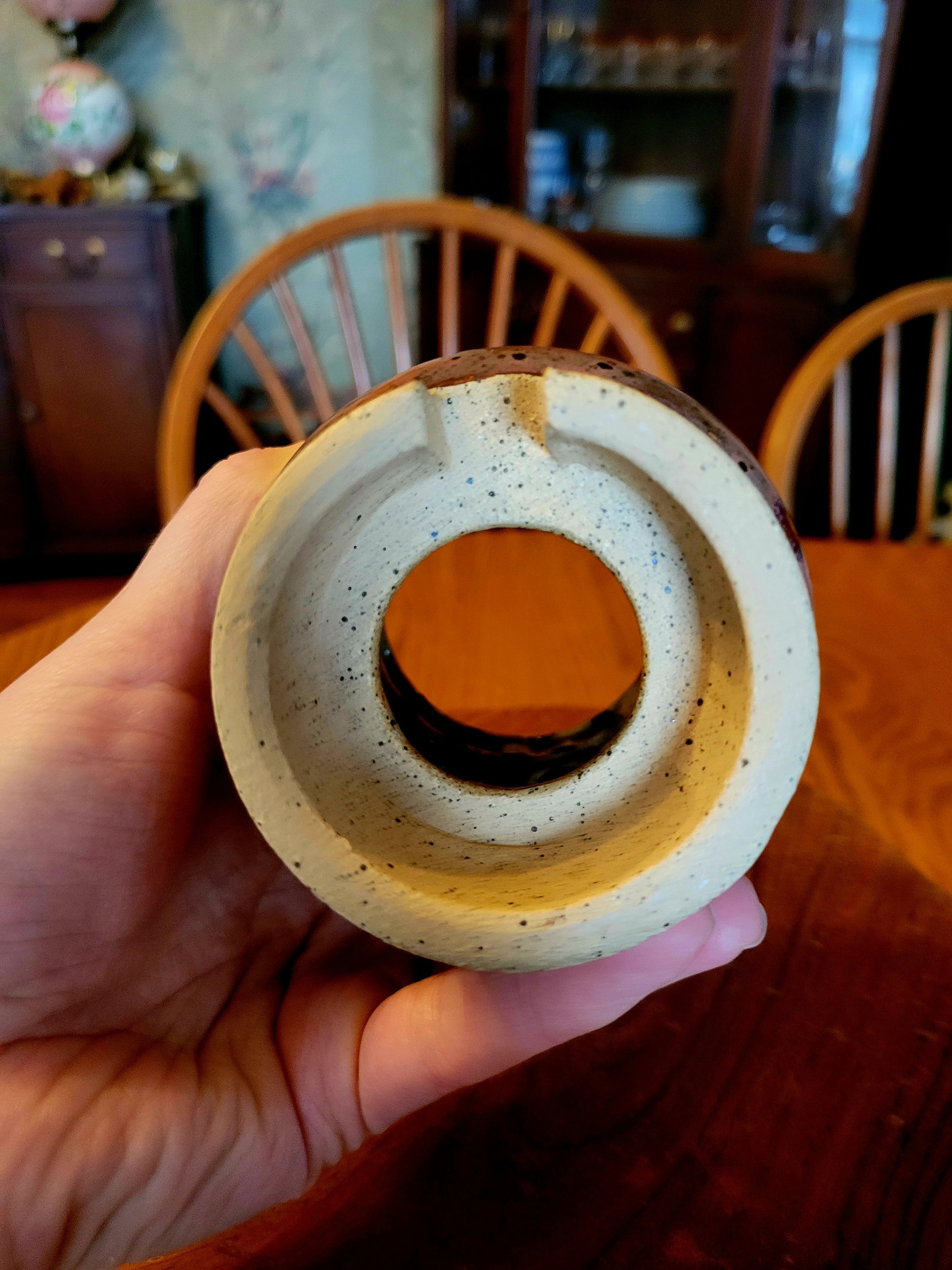 Hand holding a ceramic ring with a wooden center against a blurred indoor background