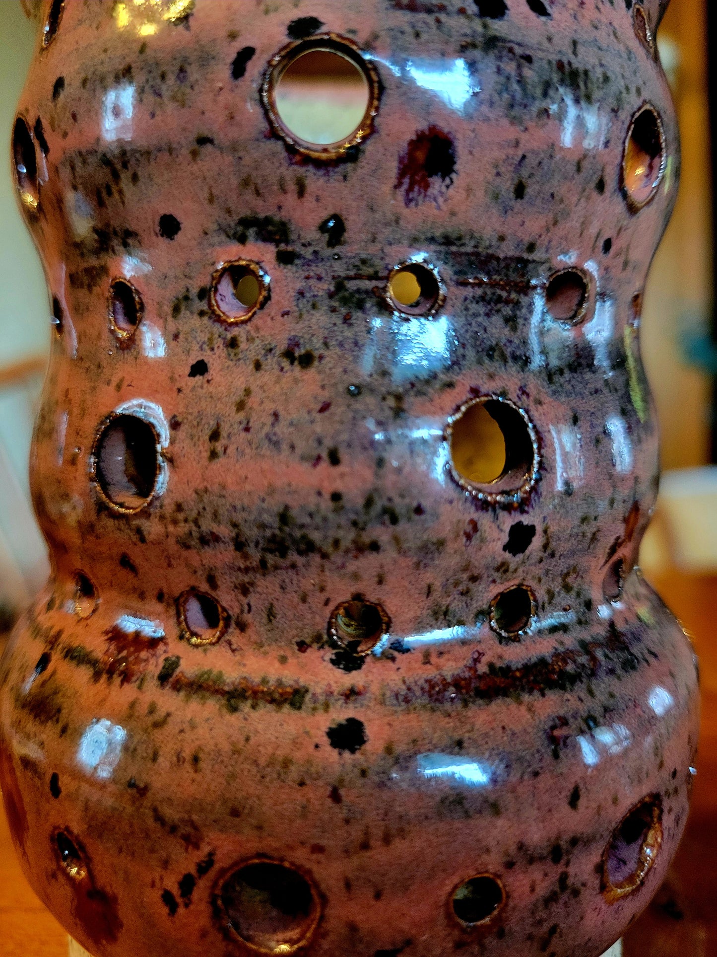 Ceramic vase with speckled glaze and circular holes on a blurred background