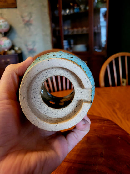 Hand holding a ceramic or stone object with concentric circles, blurred indoor background