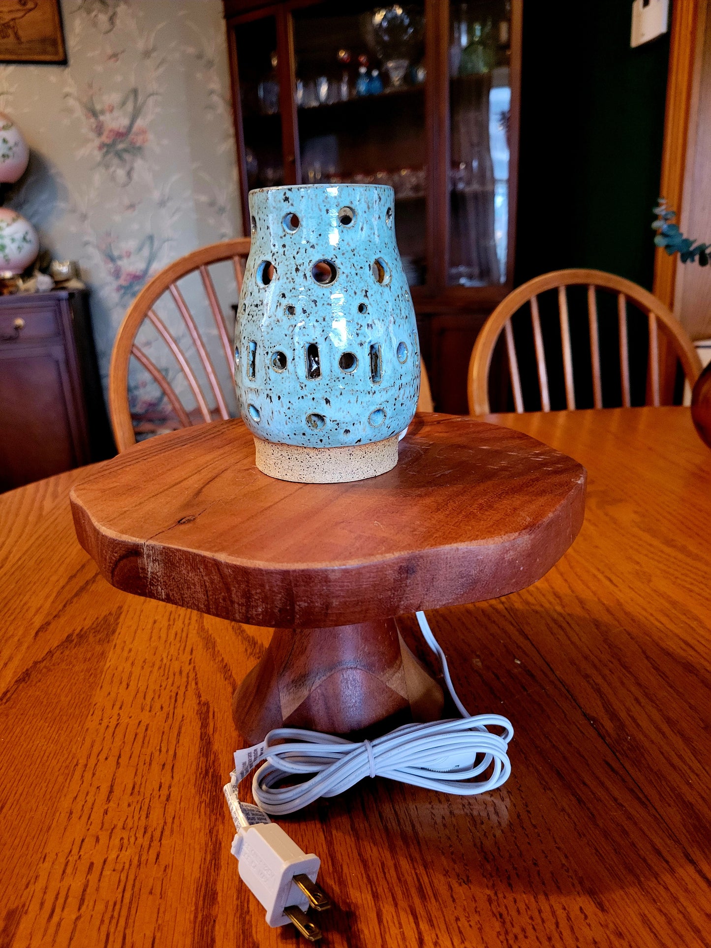 Blue ceramic lamp on a wooden stand with a visible power cord, set against a home interior background.
