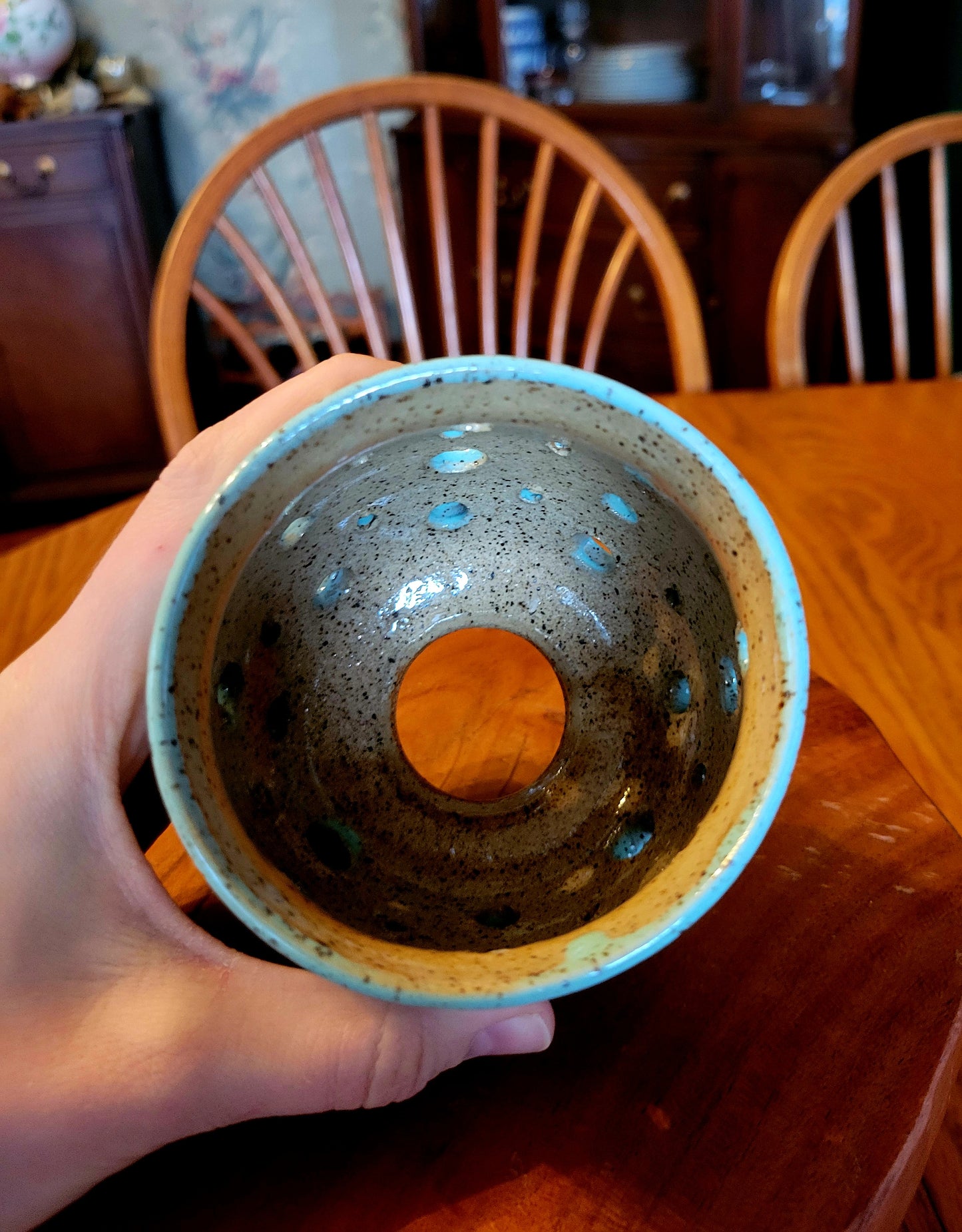 Hand holding a ceramic cup with a textured interior against a wooden chair and table background