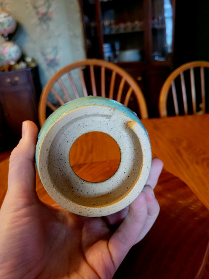 Hand holding a ceramic bowl with concentric circles against a wooden chair and table background