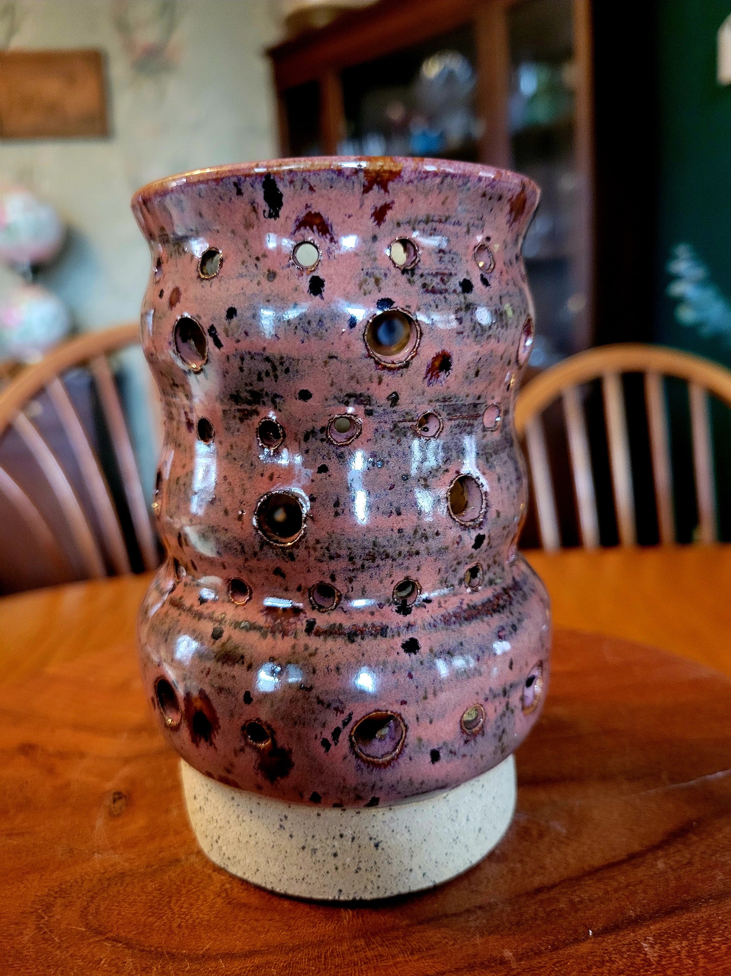 Pink ceramic vase with holes on a wooden table