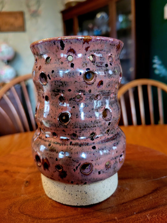 Pink ceramic vase with holes on a wooden table